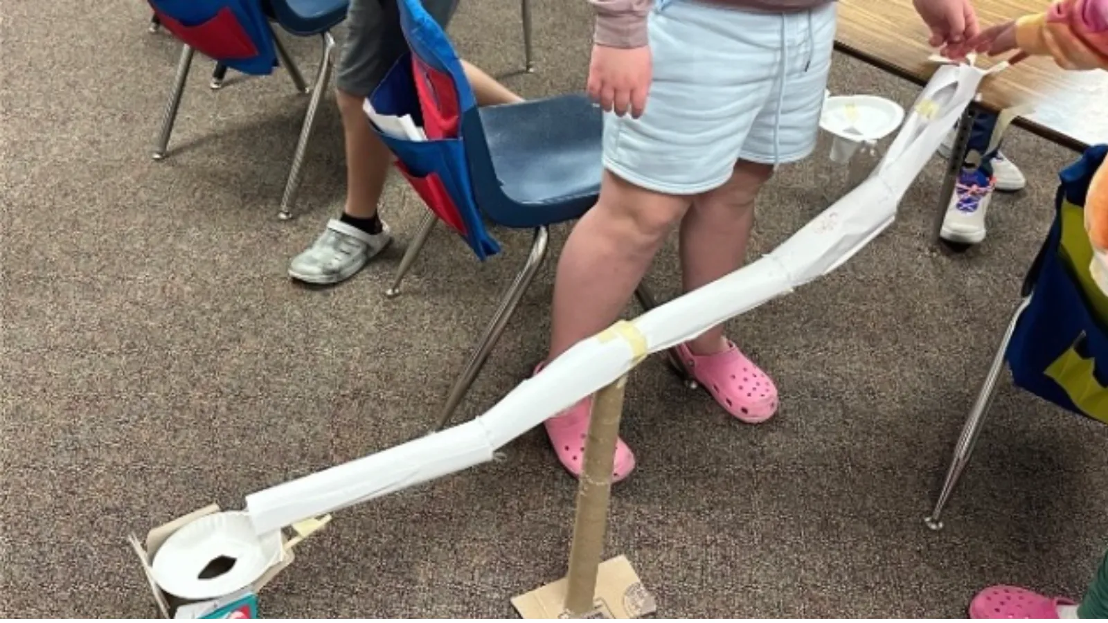 A paper roller coaster track built by an elementary student, with support beams made from paper towel rolls.