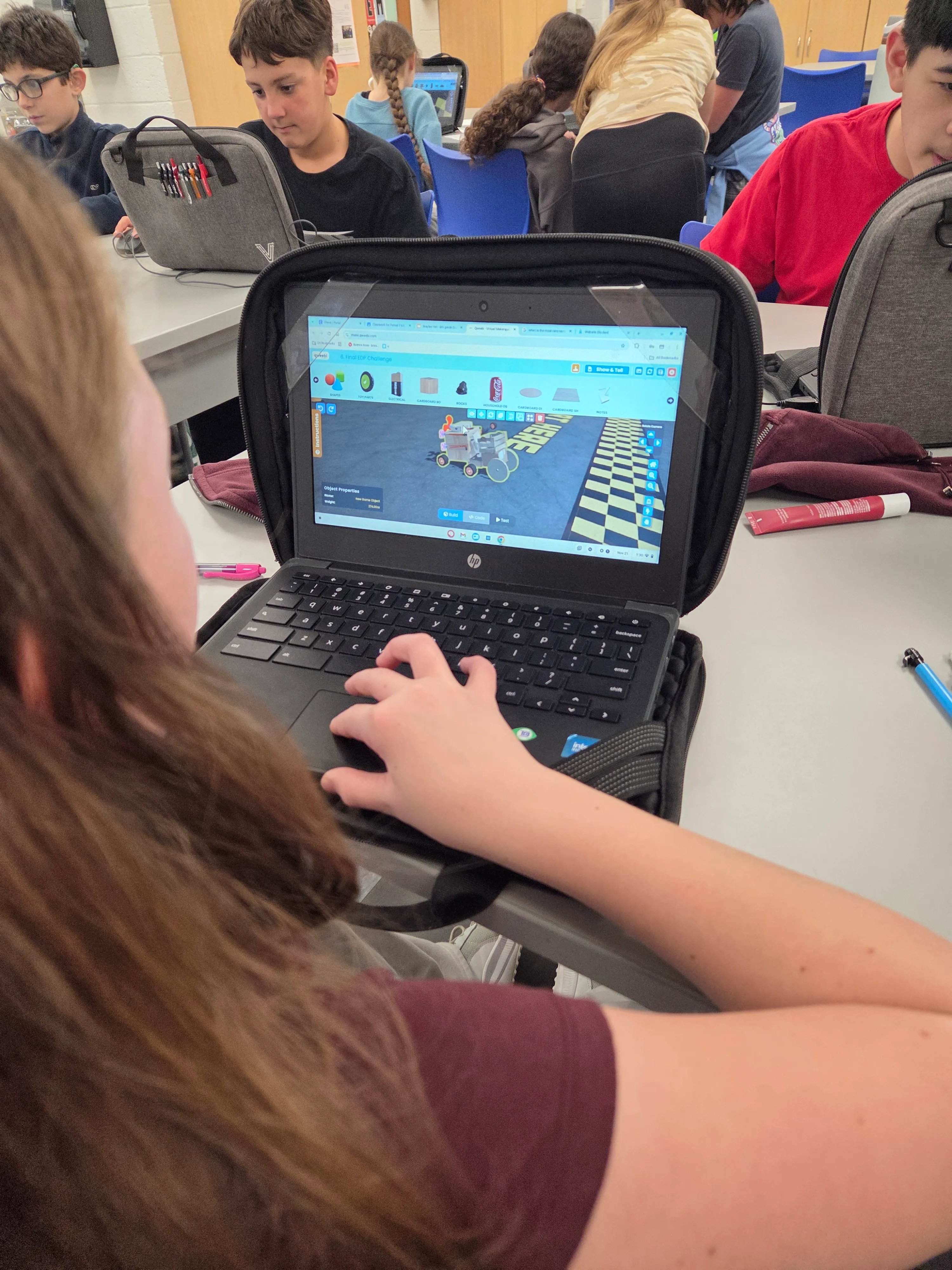 A student testing a Mars Rover build on a Chromebook, with classmates working in the background.