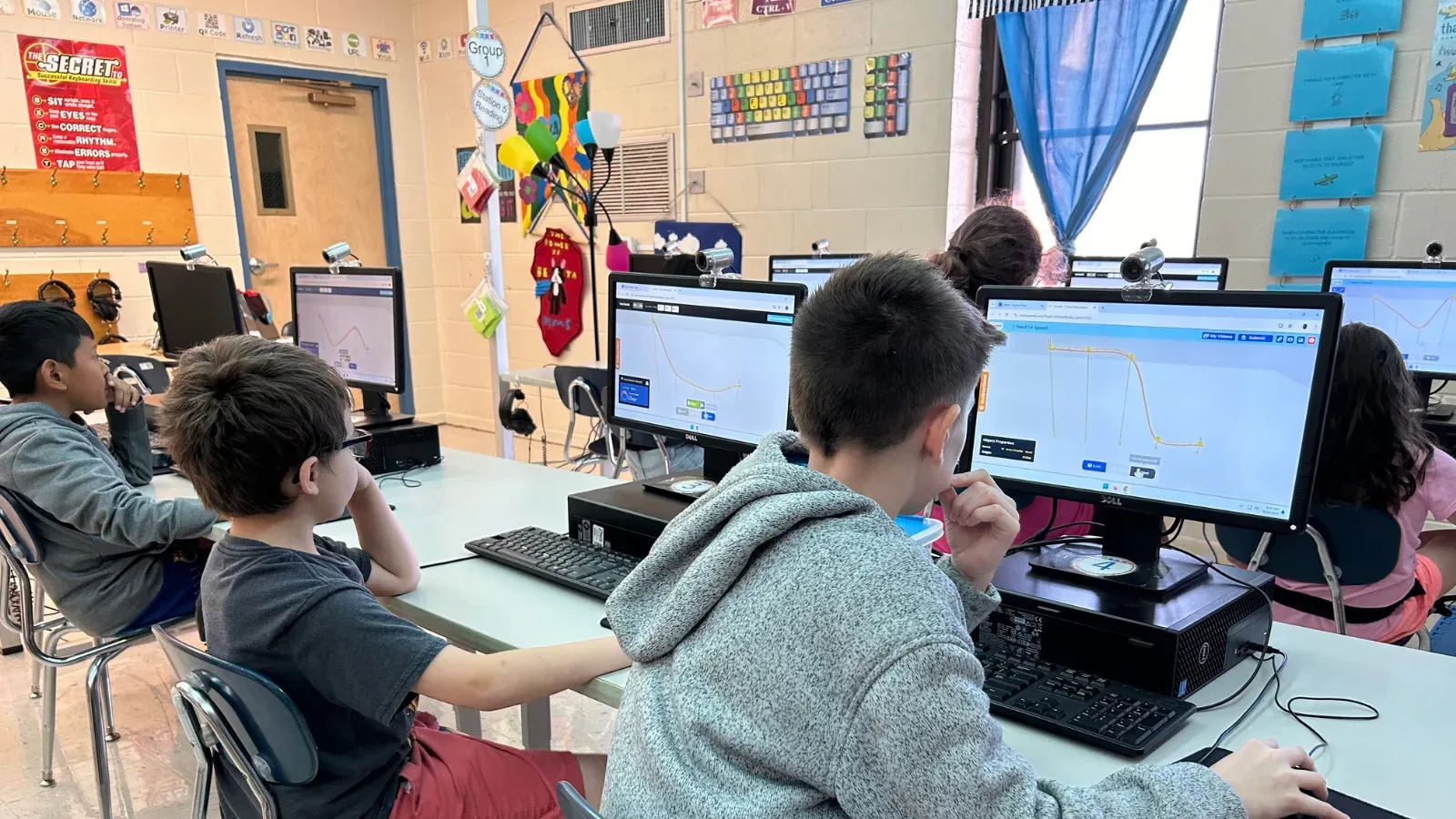 A row of students working in Qweebi at desktop computers in a school computer lab.
